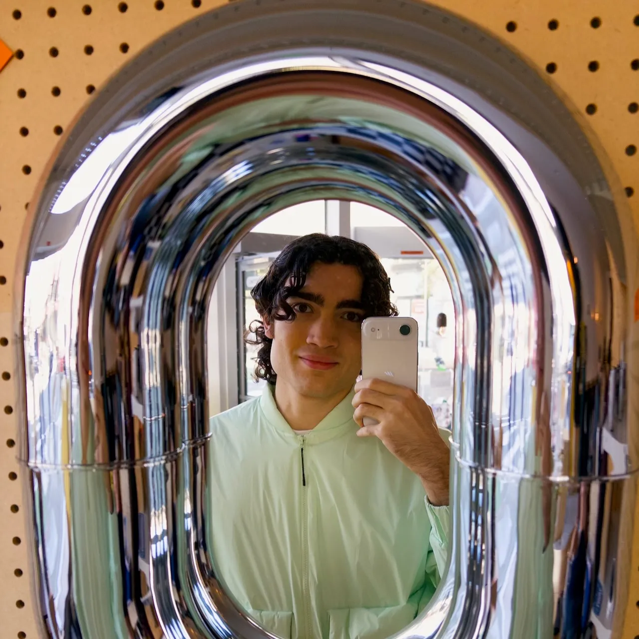 Mirror selfie of Lachlan wearing a pink raincoat in a circular mirror seamlessly blending into stainless steel