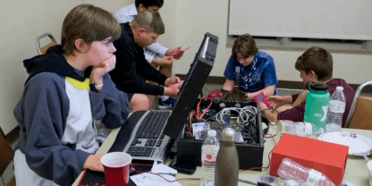 Group of teenagers with one working on a breifcase-enclosed computer in a onesie